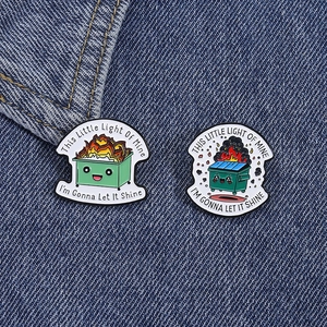 Macro detail of cartoon burning trash can enamel pins on blue denim fabric background