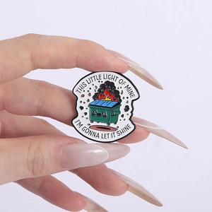 Detail showing hand holding green dumpster fire enamel pin with motivational text
