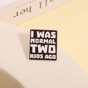 Detail of square brown enamel pin with I WAS NORMAL TWO KIDS AGO humor text