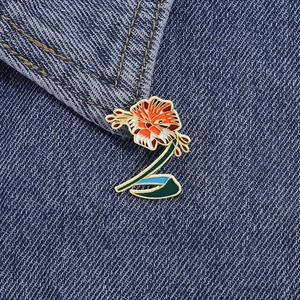 Detail einer bunten Emaille-Brosche mit Lilienmotiv am dunkelblauen Jeanskragen