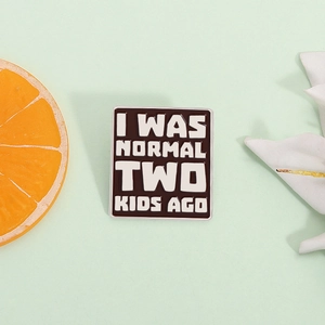 Detail of a rectangular black enamel pin with I WAS NORMAL TWO KIDS AGO humor text