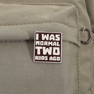 Macro shot of 'I WAS NORMAL TWO KIDS AGO' enamel pin on an olive green backpack