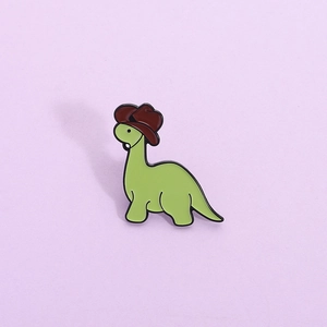 Cartoon green dinosaur enamel pin wearing a brown cowboy hat on a purple background