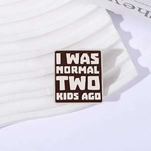Square enamel pin with I WAS NORMAL TWO KIDS AGO text on white display stand