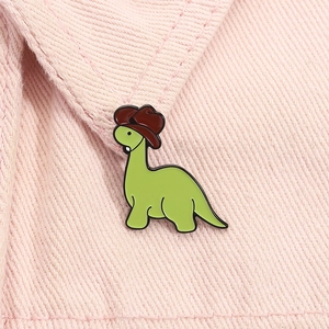 Detail of a cute green dinosaur enamel pin with a cowboy hat on pink denim fabric