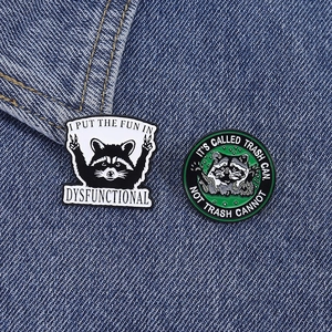 Macro shot of two creative raccoon enamel pins with funny quotes on blue denim fabric