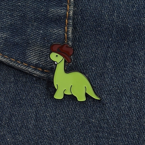 Detailed view of a green dinosaur enamel pin wearing a brown cowboy hat on denim fabric