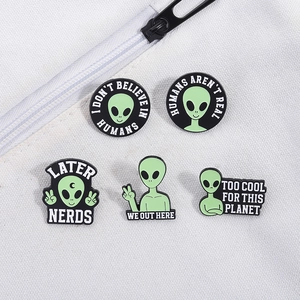 Close-up of five punk style green alien enamel pins featuring Humans Aren't Real slogan