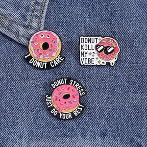 Dettaglio di tre spille smaltate a forma di ciambella rosa su denim con divertenti motti