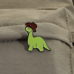 Cartoon green dinosaur enamel pin with a cowboy hat on a canvas backpack accessory