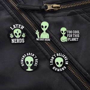 Detail of five alien enamel pins on a leather jacket with text like I Don't Believe In Humans