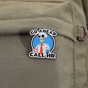 Enamel skull pin featuring a shirt and tie with Go Ahead Call HR text on a green backpack