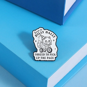 Detail of cartoon cat enamel pin with Born to Dilly Dally quote on blue gift box background