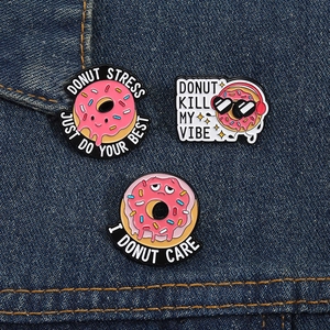 Dettaglio di tre spille smaltate a forma di ciambella con scritte su denim blu