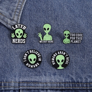 Detailed macro view of five green alien enamel pins on blue textured denim fabric