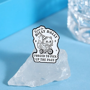 Detail of cartoon cat on tricycle enamel pin with witty quote on blue background