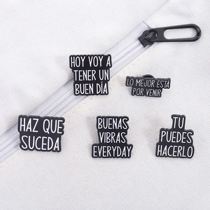Detailed close-up of five black enamel pins with Spanish quotes on a canvas bag background