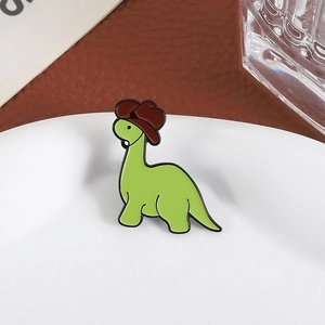 Cute green cartoon dinosaur enamel pin with a brown cowboy hat on a white plate