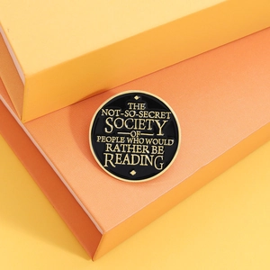 Détail d'une broche ronde en émail noir avec citation dorée sur un support orange vif