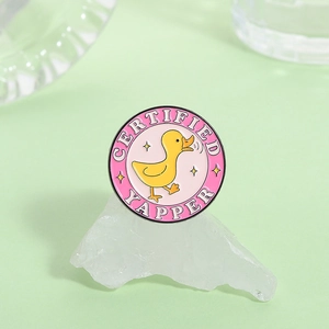 Macro dettagliata di una spilla in smalto rosa con papera gialla e scritta Certified Yapper