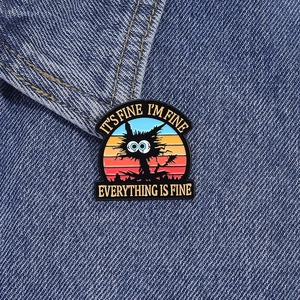 Detail of funny black cat enamel pin with retro sunset background on denim jacket collar