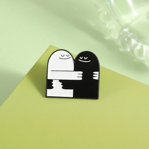 Détail de broches en émail minimalistes fantômes noir et blanc sur un support vert clair