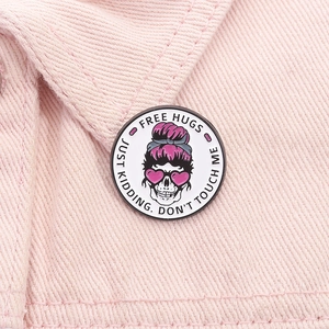 Macro shot of Free Hugs skull enamel pin with pink heart glasses on denim fabric