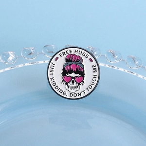 Round skull enamel pin with pink heart sunglasses and Free Hugs text on a blue tray