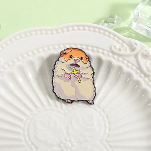 Creative enamel hamster brooch with a yellow cross, displayed on a decorative ceramic dish