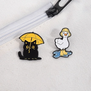 Close-up of enamel pins featuring a black cat and goose on a white canvas background