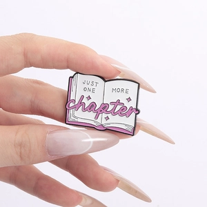 Pink enamel book brooch featuring Just One More Chapter quote held by fingers