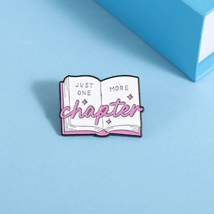 Detail of pink book enamel pin featuring JUST ONE MORE chapter text and stars