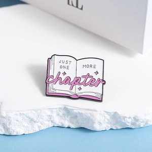 Detail of pink book enamel pin featuring Just One More Chapter literary text design