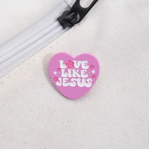 Détail d'un pin's en émail rose en forme de cœur Love Like Jesus sur toile blanche