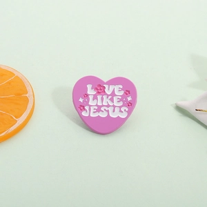 Détail de la broche émaillée en forme de cœur rose avec texte Love Like Jesus sur vert