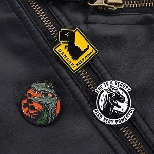 Detail of creative dinosaur enamel badges showing high-quality metallic finish on a leather jacket