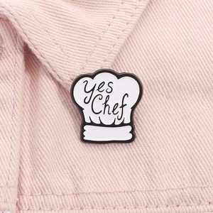Détail d'un pin's toque de chef blanc émaillé avec texte Yes Chef sur denim rose