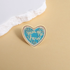Dettaglio della spilla a cuore smaltata azzurro con testo dorato You're My Hero
