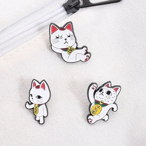 Detailed view of three funny lucky cat enamel pins on white canvas fabric background