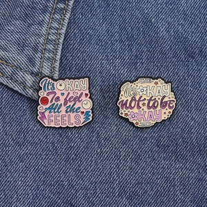 Detail of inspirational quote enamel pins on denim fabric showing metal textures