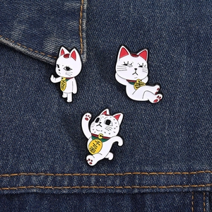 Three creative Maneki Neko enamel pins set on denim, showing funny lucky cat poses
