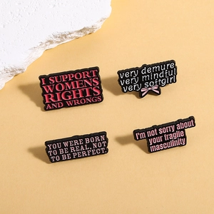 Dettaglio di quattro spille in smalto nero con citazioni e scritte rosa su sfondo beige