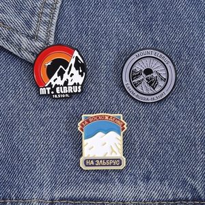 Trois pin's émaillés du mont Elbrus avec sommets et symboles de randonnée sur tissu denim