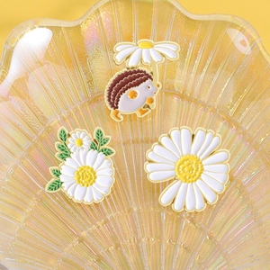 Detailed close-up of cute hedgehog and daisy enamel pins set on a yellow shell tray