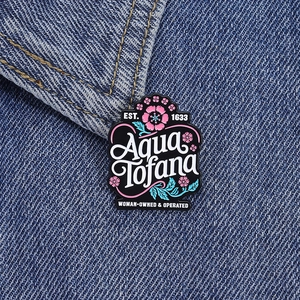 Detailed macro view of Aqua Tofana enamel pin with pink flowers on denim fabric