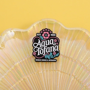 Detailed macro view of the Aqua Tofana enamel pin with floral patterns on a shell tray