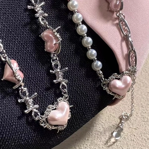 Close-up of pink heart pendants with silver barbed wire chain and faux pearl details