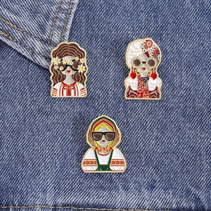 Détail de trois broches en émail créatives épinglées sur un fond en tissu denim bleu foncé