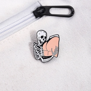Detail of funny punk skull and pink butt enamel pin on a white canvas zipper bag