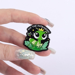 Cartoon green praying mantis enamel pin with Eat The Patriarchy slogan on black background